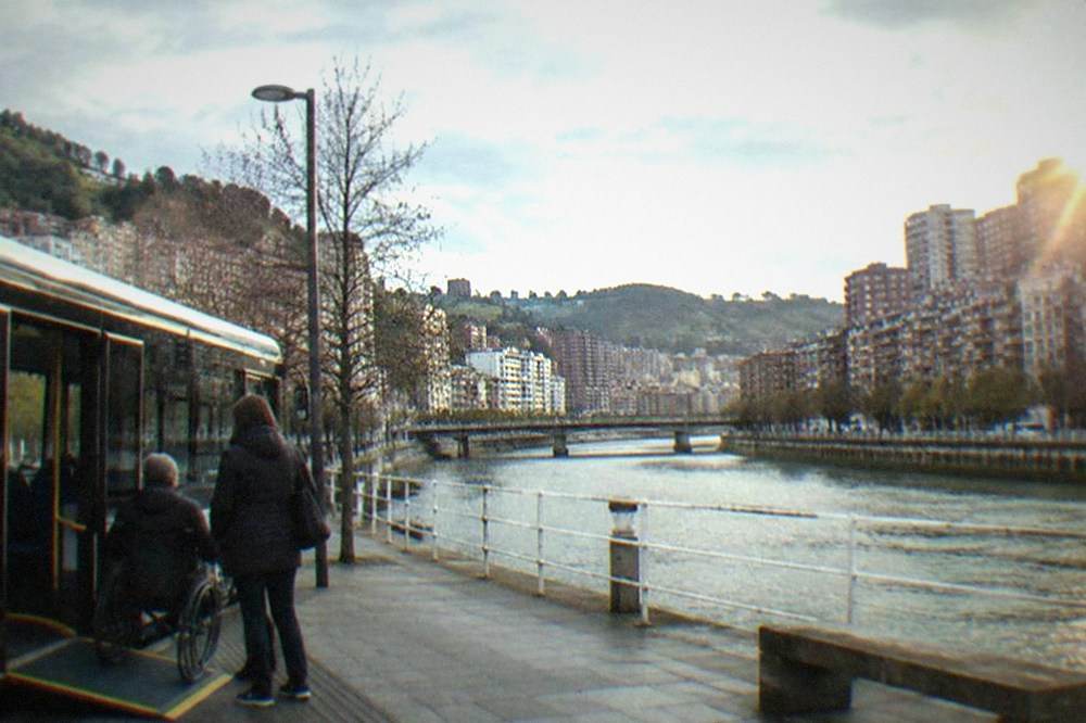 Low-floor city bus with a deployed wheelchair ramp at a stop in central Bilbao