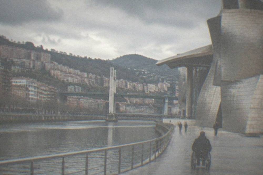 Wheelchair user crossing a smooth riverside plaza toward the titanium curves of the Guggenheim
