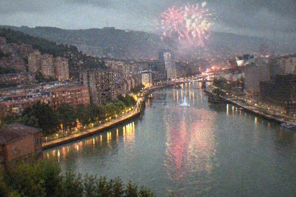 Fireworks bursting in colours above a city skyline at night with a river reflecting the light