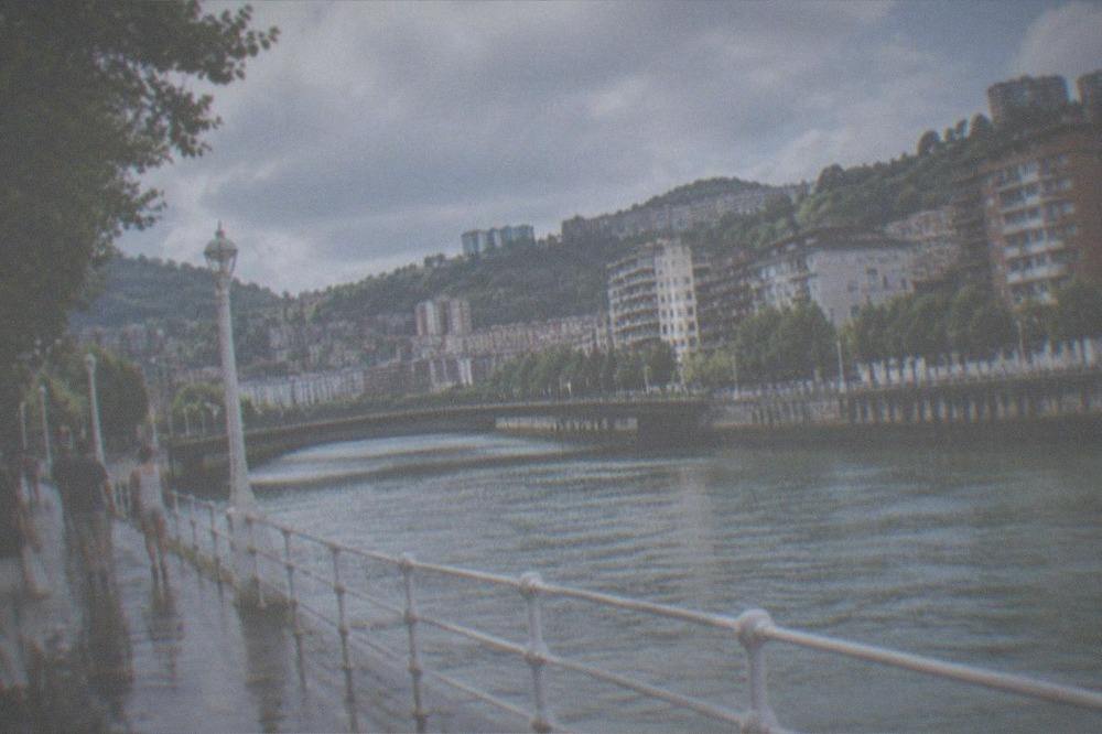 People in light summer clothing walking along a riverside promenade under a partly cloudy sky