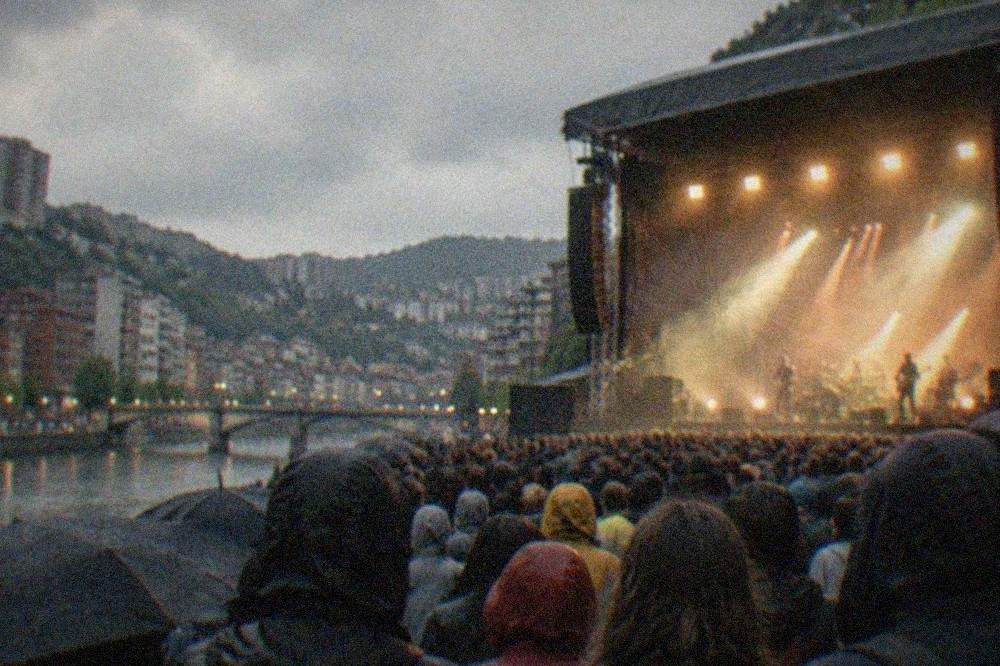 Festival main stage lit up at night with a dense crowd and haze above the stage lights