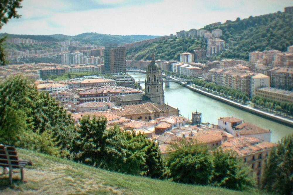 View over red rooftops and a church tower in central Bilbao from a hillside park on a clear afternoon