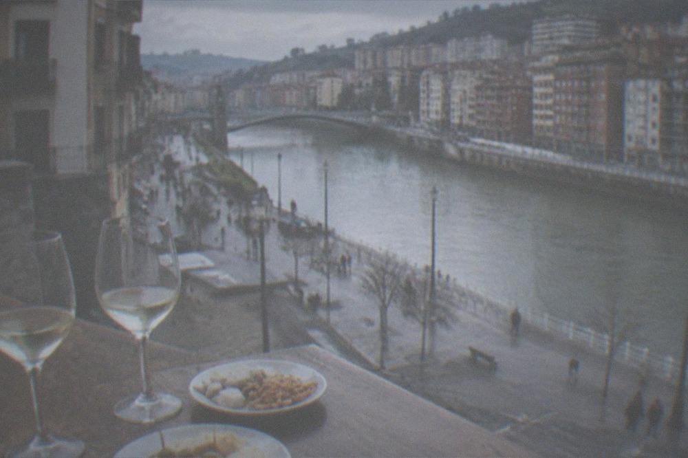 Small plates and glasses of txakoli arranged on a wooden bar top in an old town square