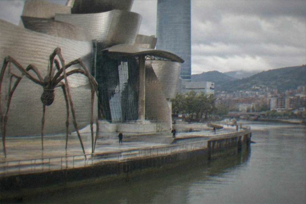 Titanium-clad museum building beside a river with a large spider sculpture in the foreground