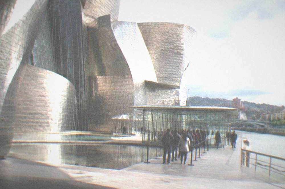 Visitors queuing at the glass ticket pavilion outside the Guggenheim Museum Bilbao on a bright morning