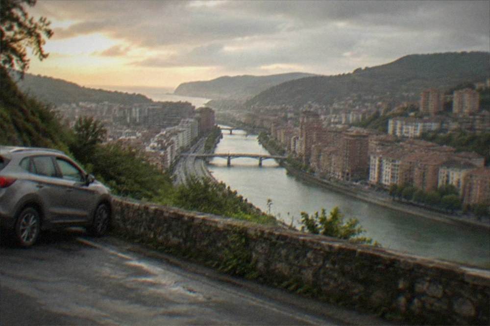 A rental car parked on a coastal road above the Bay of Biscay with green hills behind