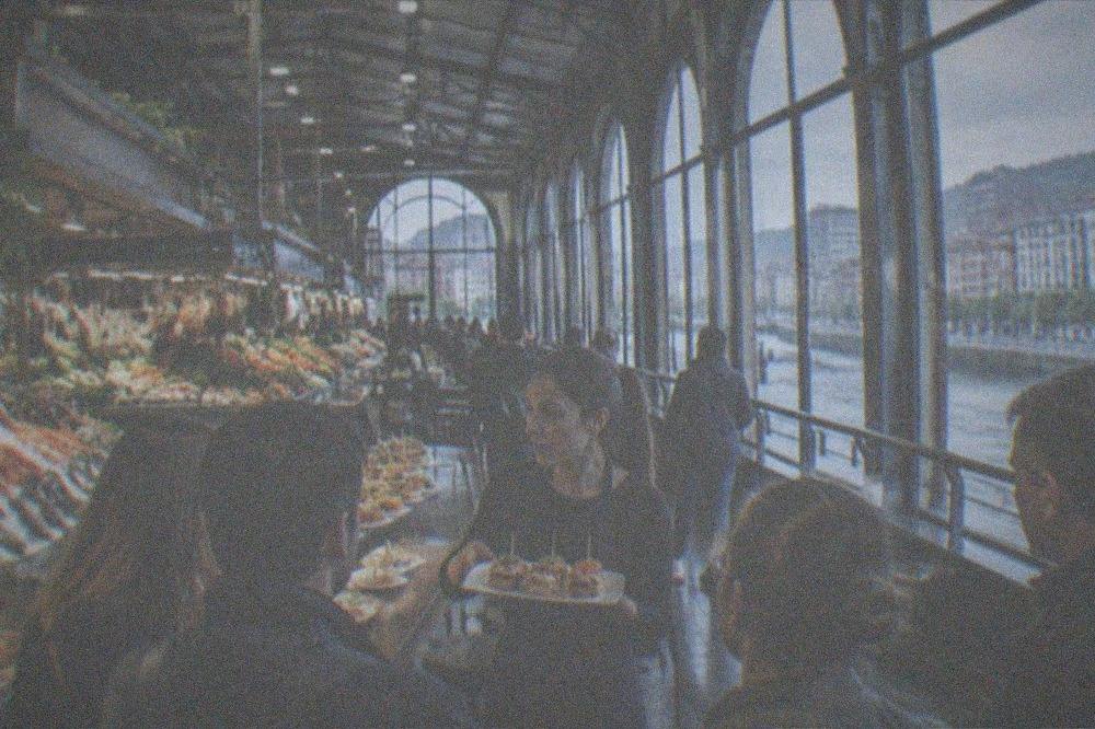 A guide presenting a plate of pintxos to a small group standing at a bar counter