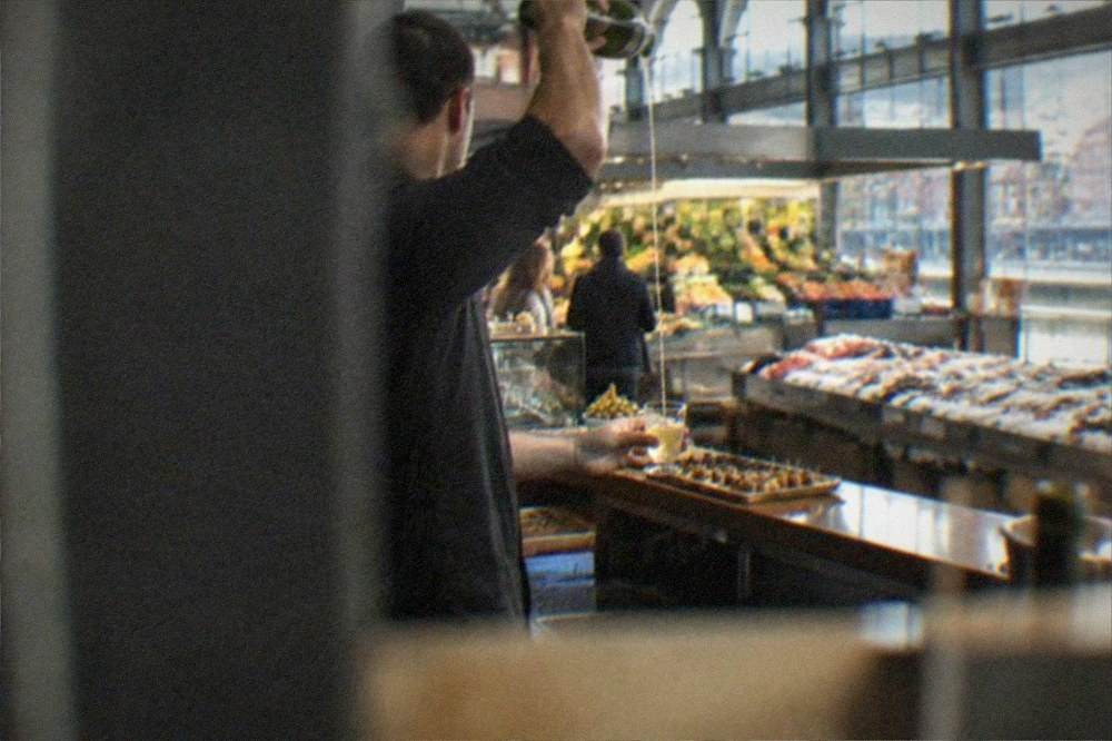 A bartender pouring txakoli wine from a height into a small glass