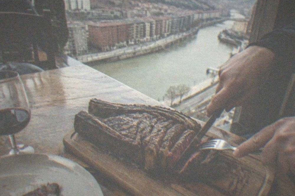 A large grilled txuleta steak being sliced at a Basque asador table