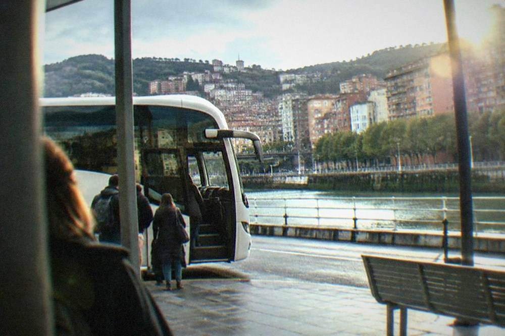 A white Bizkaibus parked at a stop outside the terminal with boarding passengers