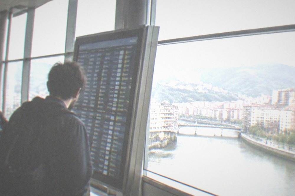 A traveler reading an information board inside the small departures hall of Bilbao Airport