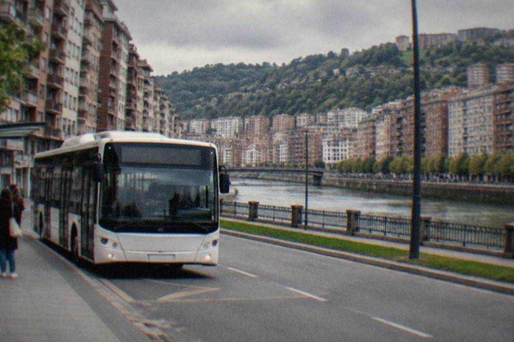 A white Bilbao city bus waiting at a stop on a wide avenue with apartment buildings behind