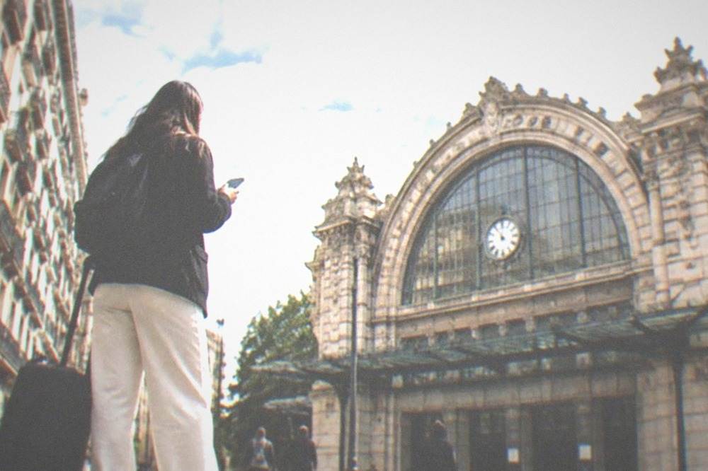 A traveler with a rolling suitcase consulting a phone on a European city street