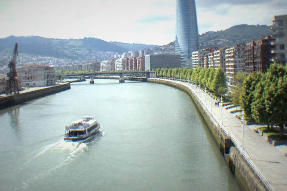 Tall glass office tower rising above the Nervion riverfront in Bilbao