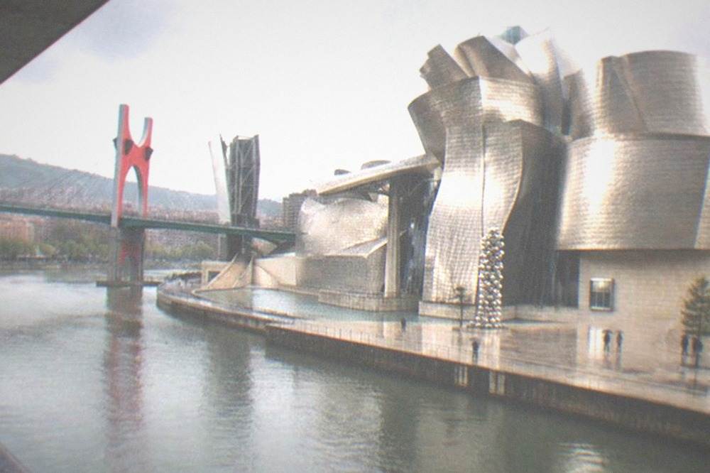 Red steel ramps of a road bridge beside a modern museum building on the river
