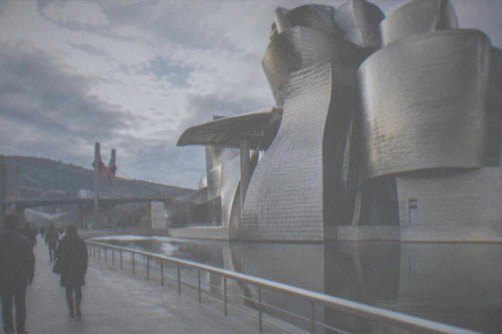 Visitors walking along a riverside promenade toward a modern museum building