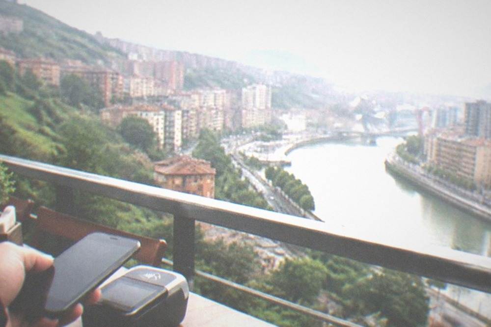 A hand holding a smartphone near a contactless payment terminal on a Bilbao terrace