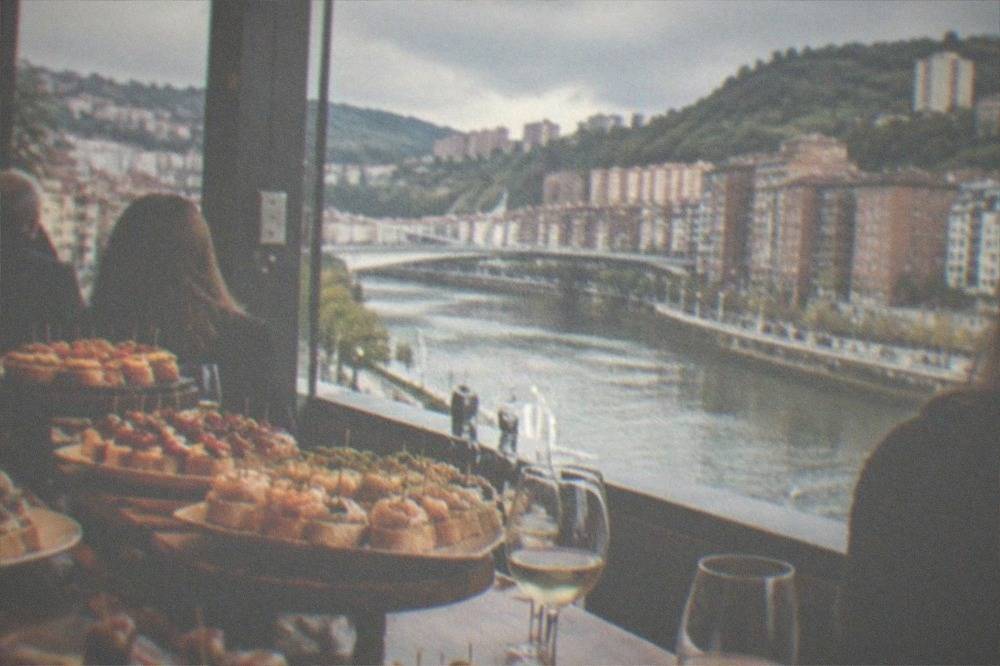 A crowded pintxos bar counter in Bilbao loaded with small skewered bites and glasses of txakoli