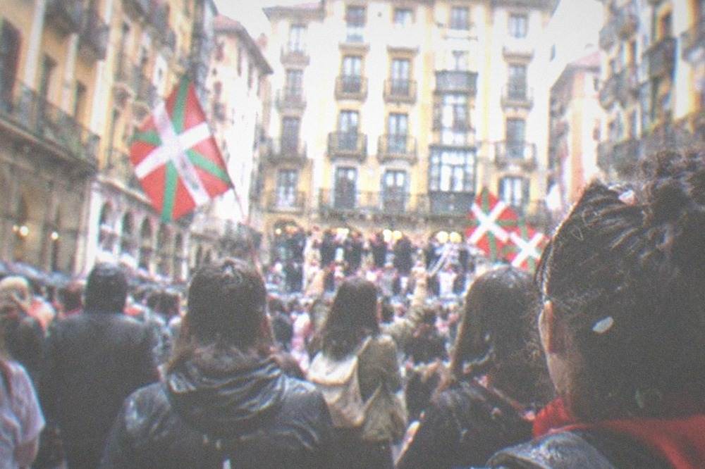 Crowds celebrating at an outdoor Basque festival with flags and confetti in a city square