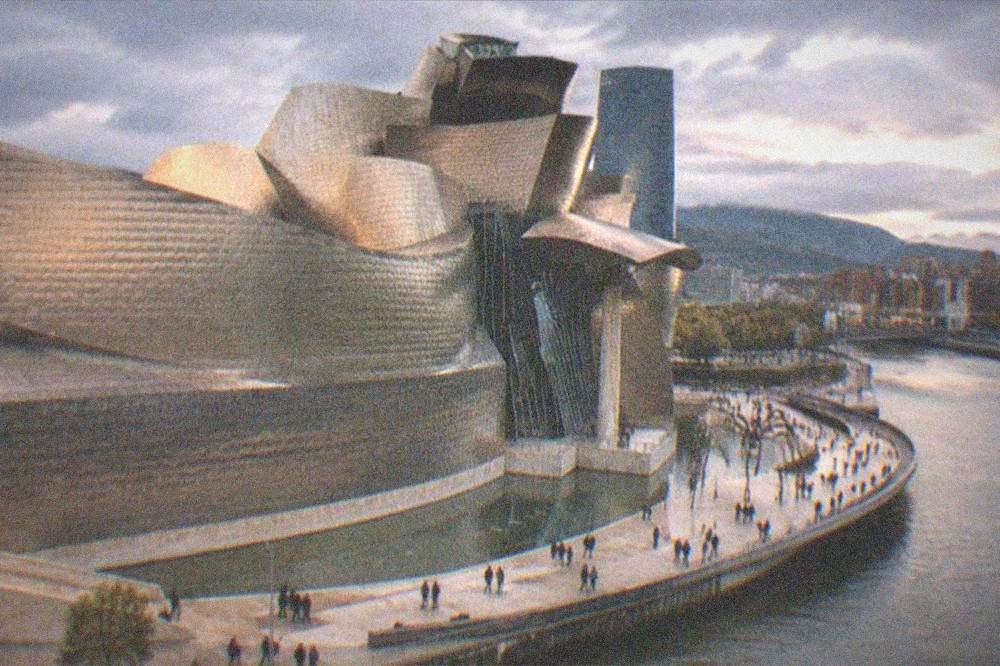 Evening light on Bilbao's Guggenheim Museum beside the estuary with people walking along the riverside