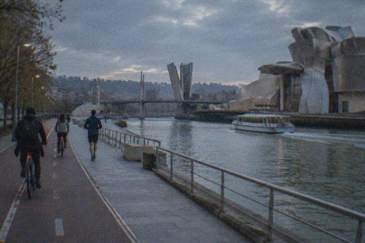 Cyclists riding a shared bike path along the Nervion river in Bilbao with the Guggenheim Museum in the background