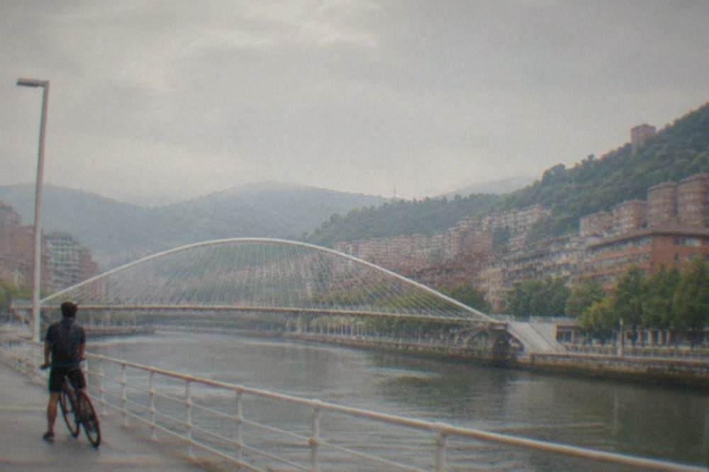 A cyclist pausing on the riverside promenade beside the Zubizuri footbridge in central Bilbao
