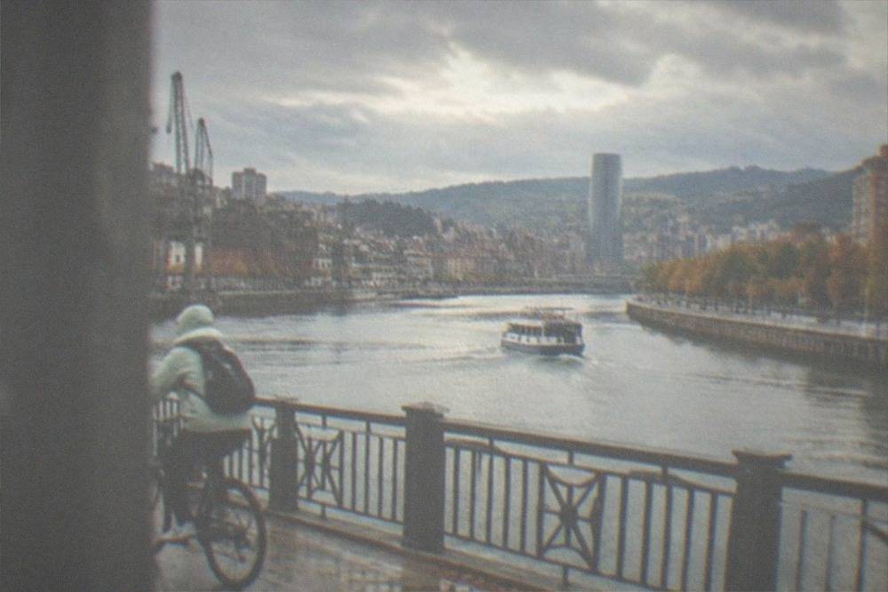 A cyclist in a light rain jacket crossing a bridge over the Nervion river in Bilbao in autumn