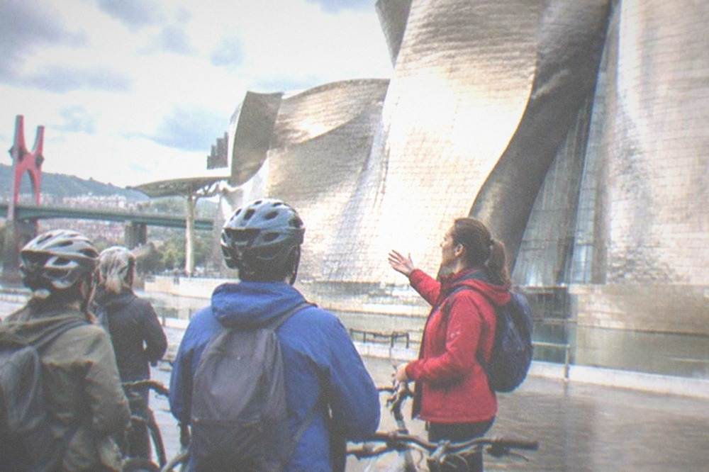 A small group of e-bike tourists listening to a guide beside the Guggenheim Museum in Bilbao