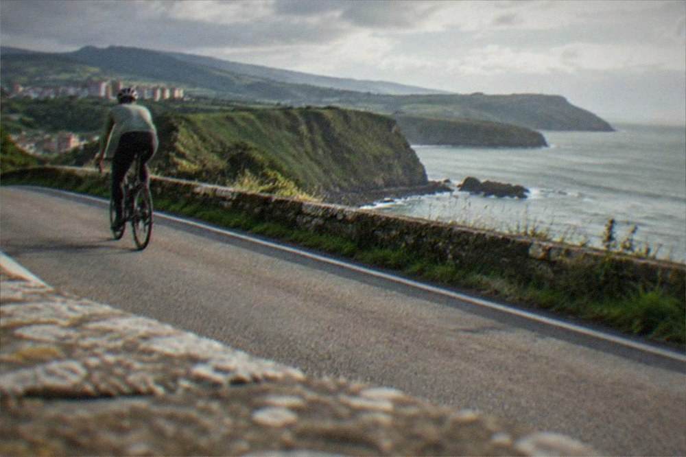 A cyclist on a coastal road above the Bay of Biscay with green cliffs and the ocean beyond near Bilbao
