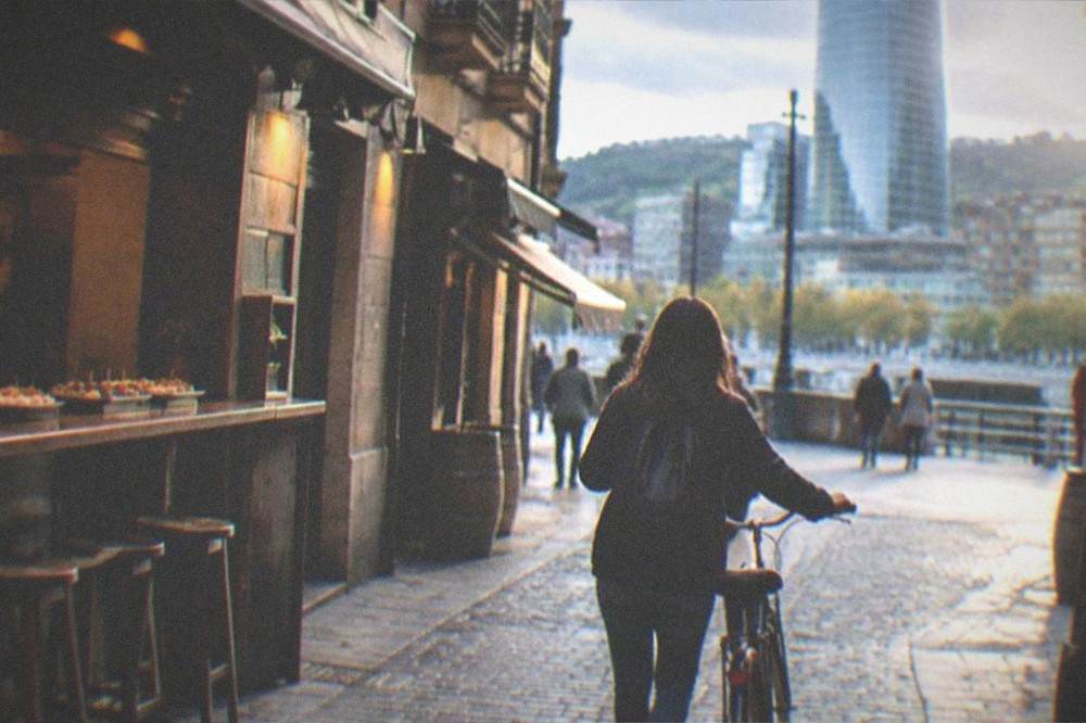 A cyclist walking a bike through a narrow cobbled street in Bilbao's old town past pintxos bars