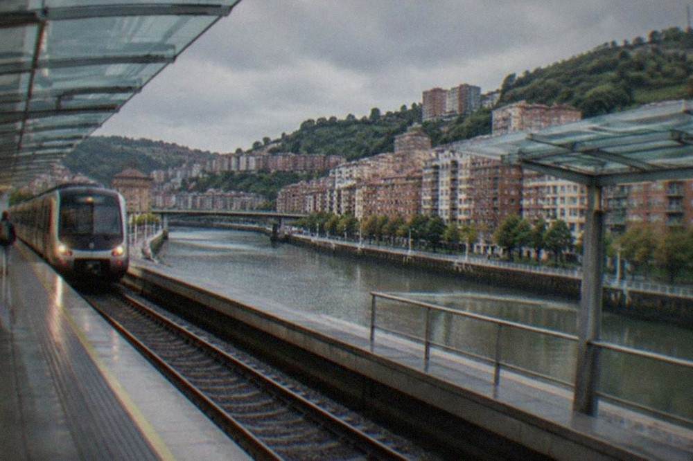 A metro train arriving at a modern Bilbao metro station with glass canopies over the platforms