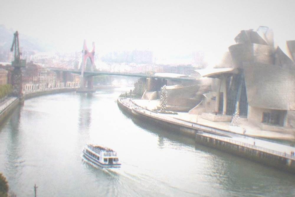 The curved titanium exterior of the Guggenheim Museum Bilbao beside the Nervion river on a bright afternoon