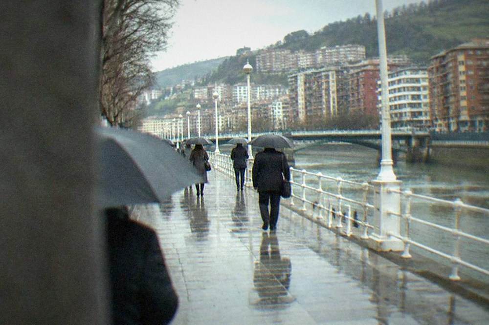 Business travelers with umbrellas walking along the Gran Via in Bilbao under overcast skies