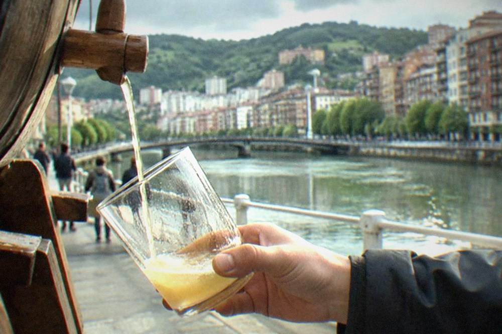 A stream of cider pouring from a barrel tap into a tilted glass held by a visitor