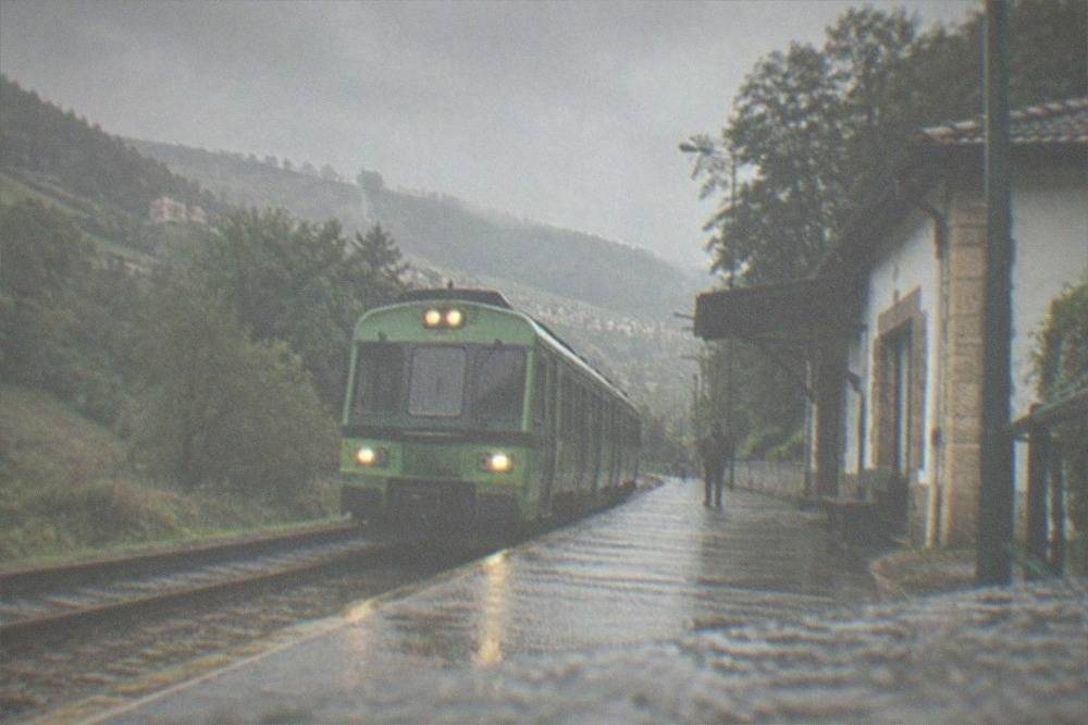A green Euskotren train at a small rural station in the Basque hills