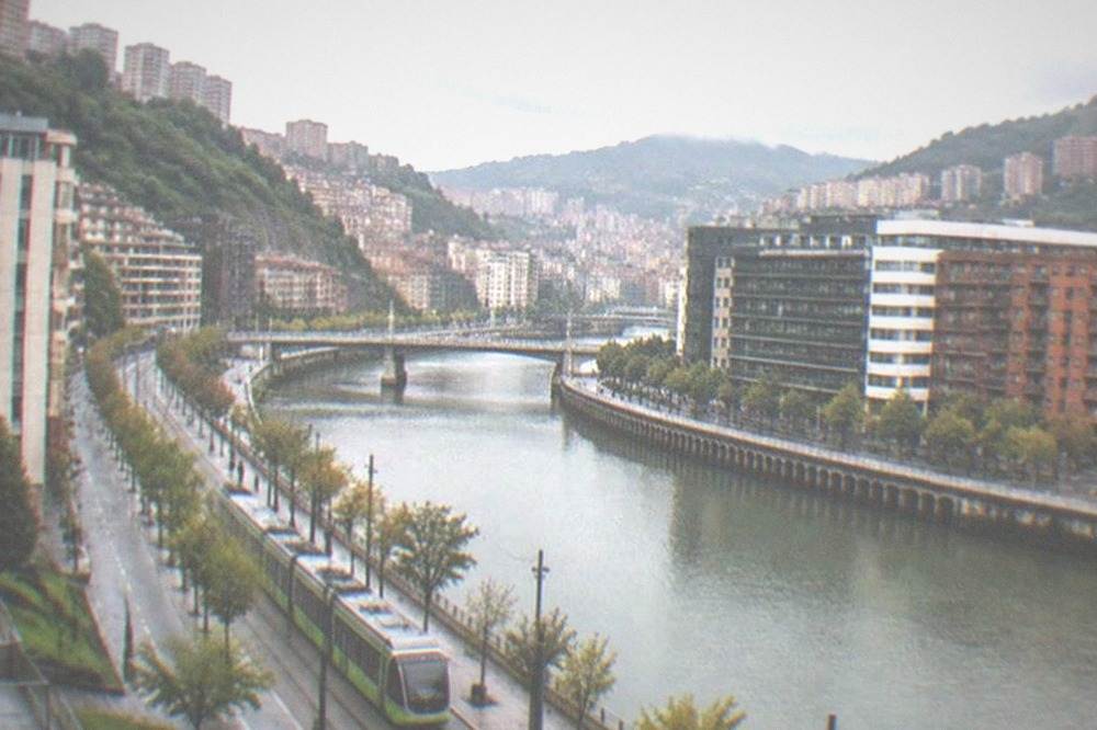 A Bilbao tram passing modern buildings along the river on a morning