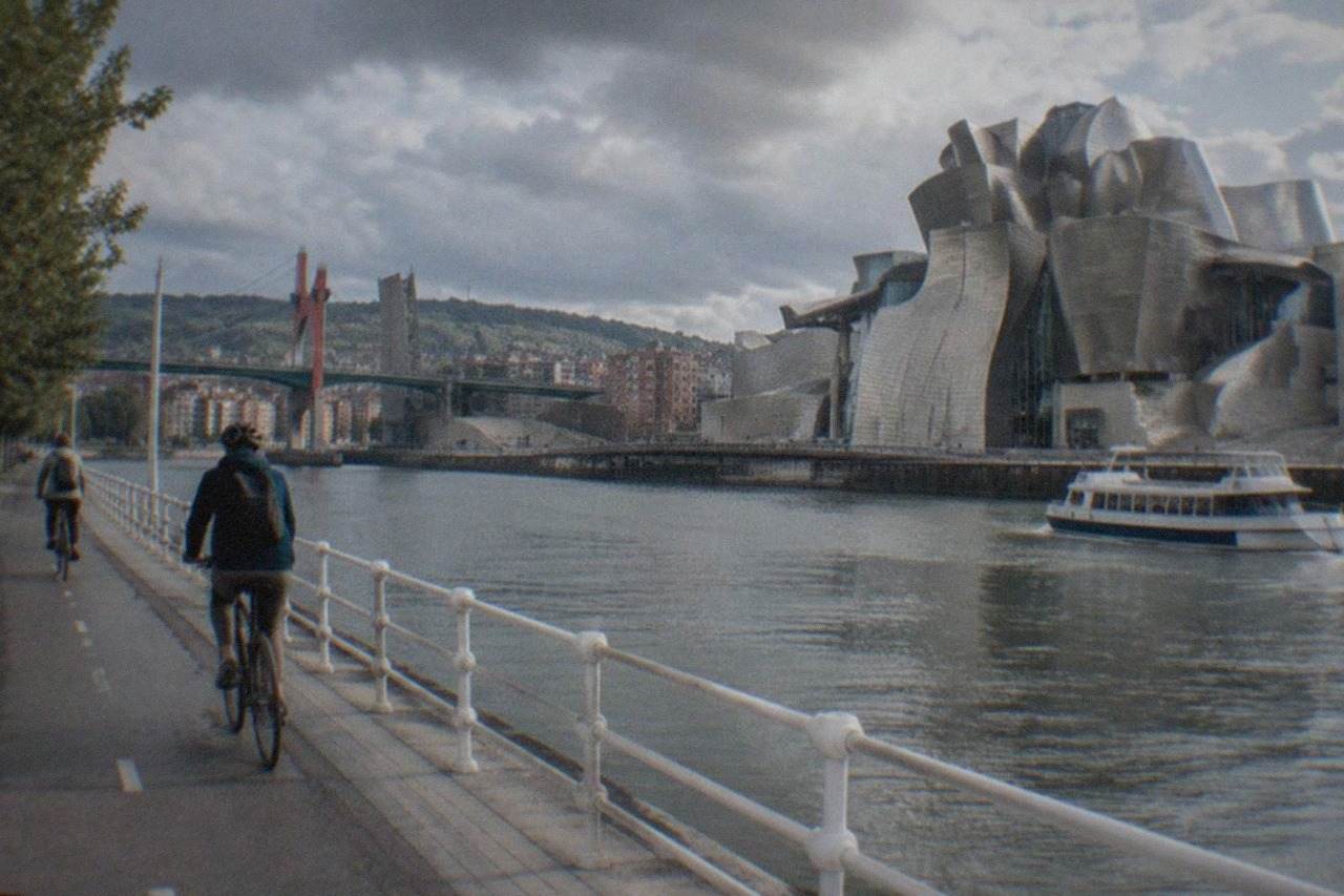 Cyclists riding along a riverside path beside the Nervion estuary with the Guggenheim Museum in the background