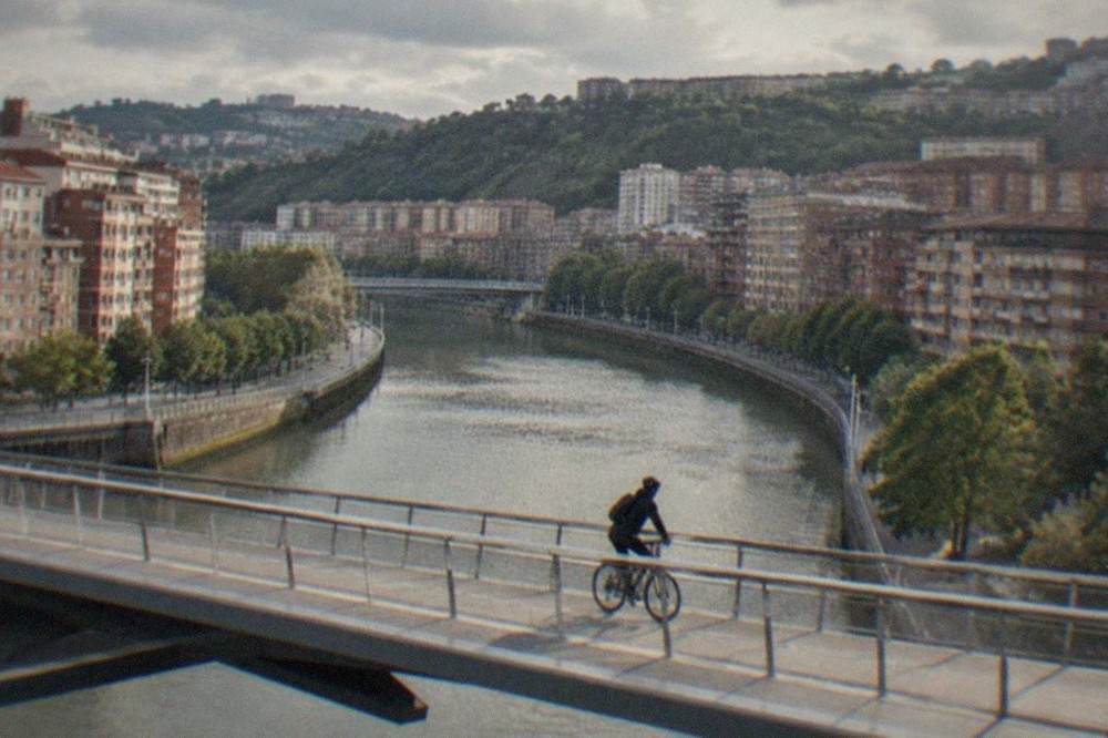 A cyclist crossing a modern footbridge over the Bilbao estuary on a bright morning