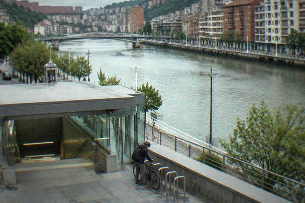 A cyclist locking a bicycle beside a metro station entrance in Bilbao
