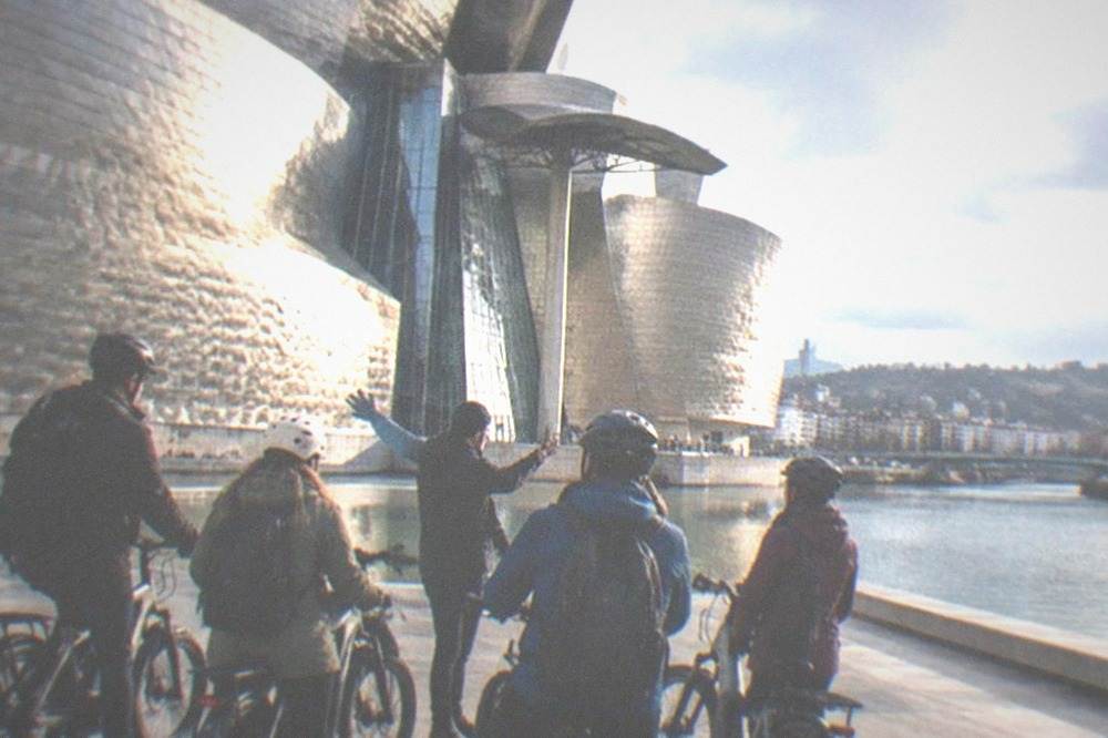 A small group of e-bike riders listening to a guide beside the titanium-clad Guggenheim Museum