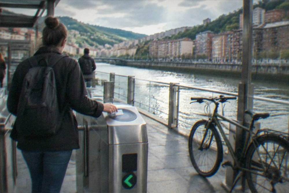 A commuter tapping a transit card at a metro station gate in Bilbao with a bicycle parked nearby
