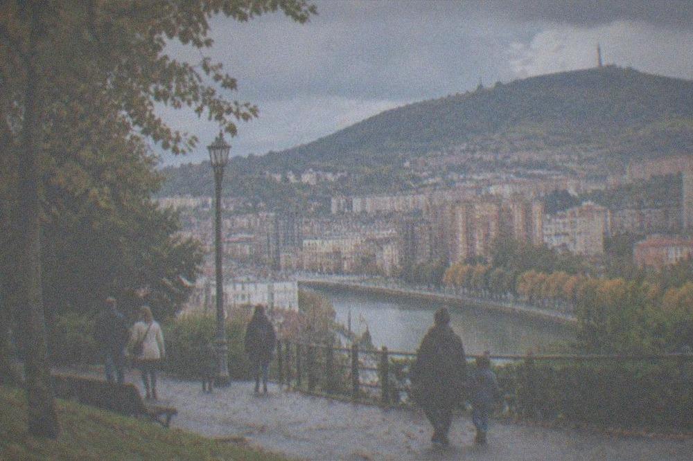 Families walking through an autumn park in Bilbao with the Artxanda hills behind the city