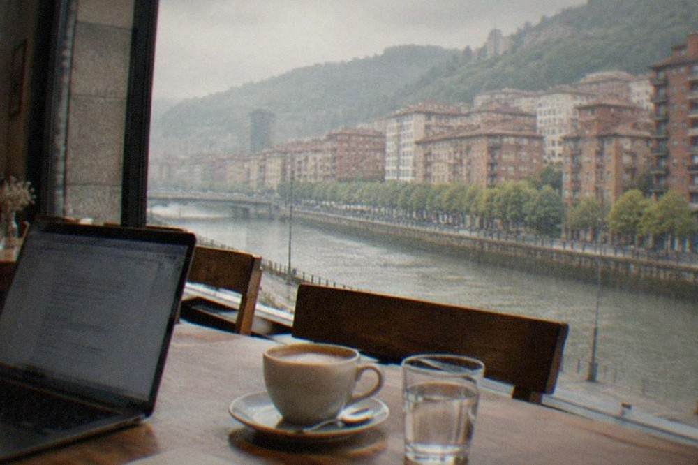 A quiet cafe interior in Bilbao with wooden tables, morning light and a laptop open beside a coffee cup