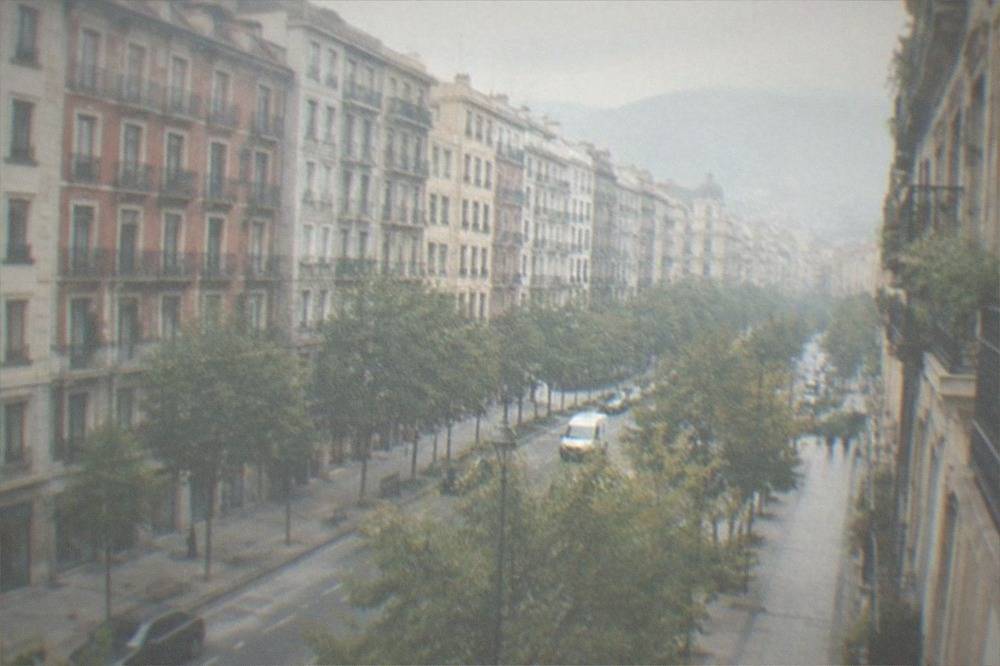 A residential street in the Ensanche district of Bilbao with apartment buildings, trees and a person walking with a backpack
