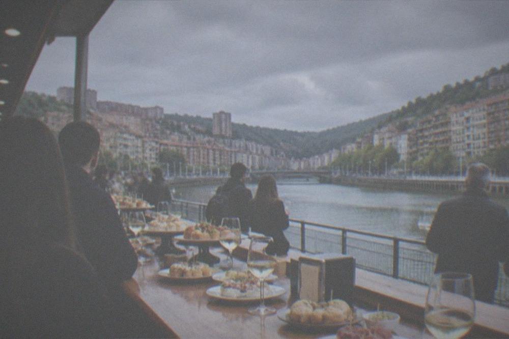 A pintxo bar counter in Bilbao crowded with small plates, glasses of txakoli wine and standing customers