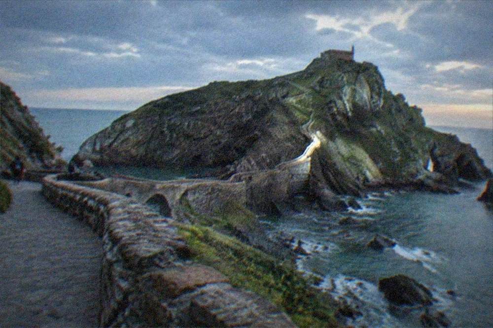 The stone causeway and hermitage of San Juan de Gaztelugatxe on a rocky islet along the Basque coast under a partly cloudy sky