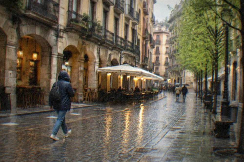 A walker in a rain jacket crossing a wet cobbled street in the Casco Viejo with cafe lights reflecting on the stones