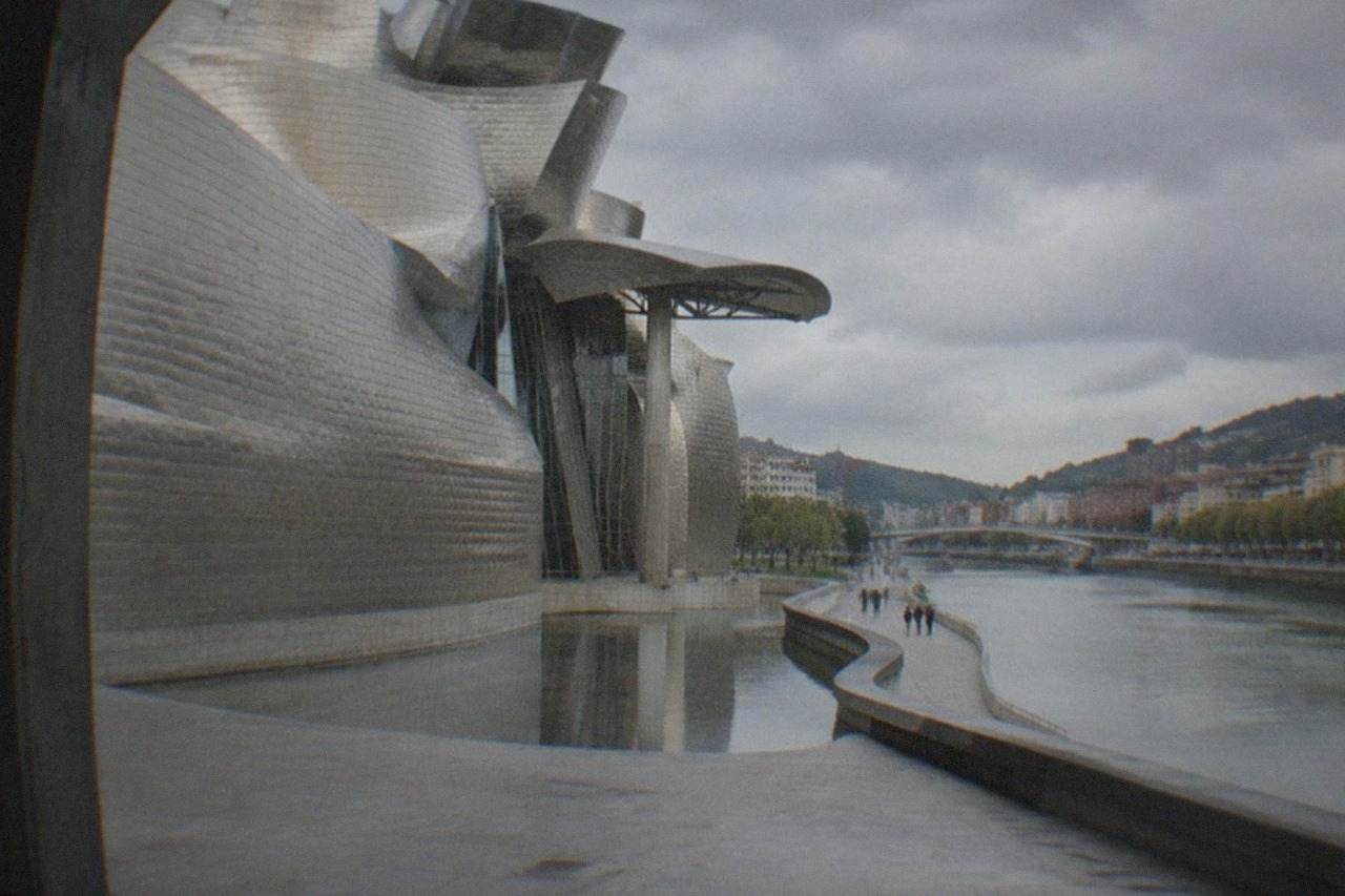 A quiet Bilbao street with the Guggenheim Museum titanium curves rising behind the Nervion river