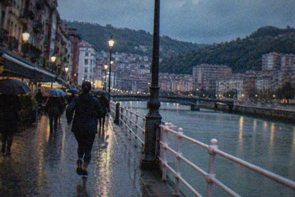 Rain-slicked cobbled street in Bilbao's Old Town with cafe awnings and pedestrians with umbrellas