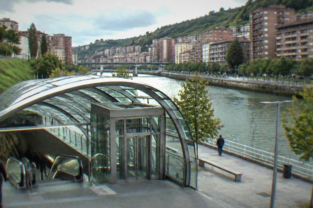 A Bilbao metro station entrance with escalators and elevators visible under the curved canopy